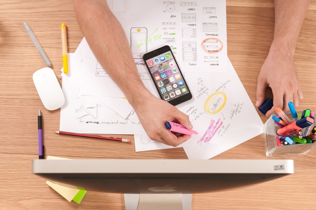 Hands planning a user experience with sketches and phone apps, representing strategic website layout decisions.